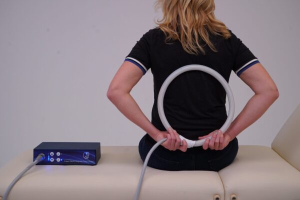 Woman applies loop applicator from TeslaFit Plus 2 to her back for PEMF Treatment
