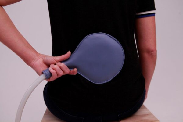 Woman applies Paddle Applicator to her back for PEMF Therapy