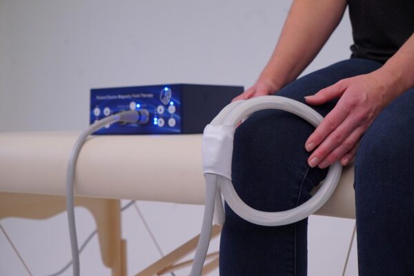 Woman sitting using TeslaFit Duo and butterfly coil on her knee