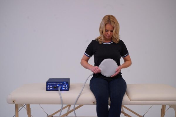 Woman sitting on table while using TeslaFit Duo and Paddle Applicator on her stomach