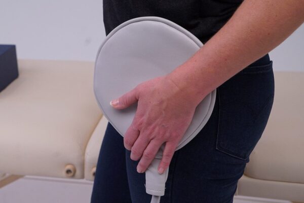 Woman applies PEMF paddle applicator on hip