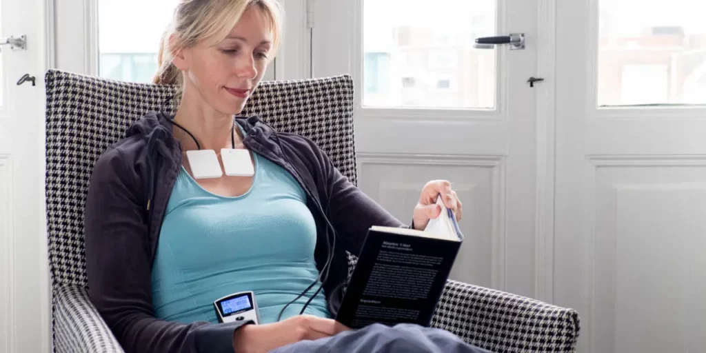 Women sits and reads a book while PEMF Device is on her waist and applied to her chest