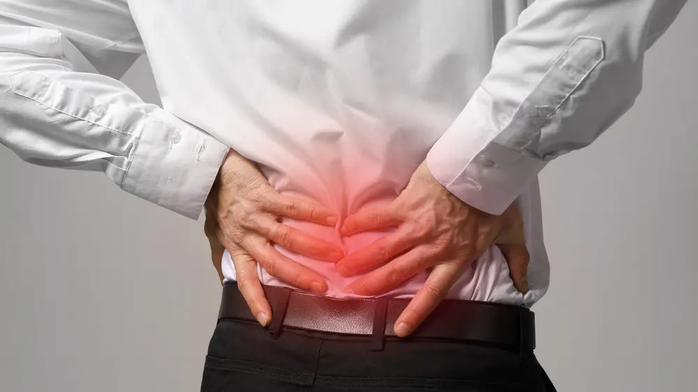 Man holds his back in pain with inflamed area shaded red