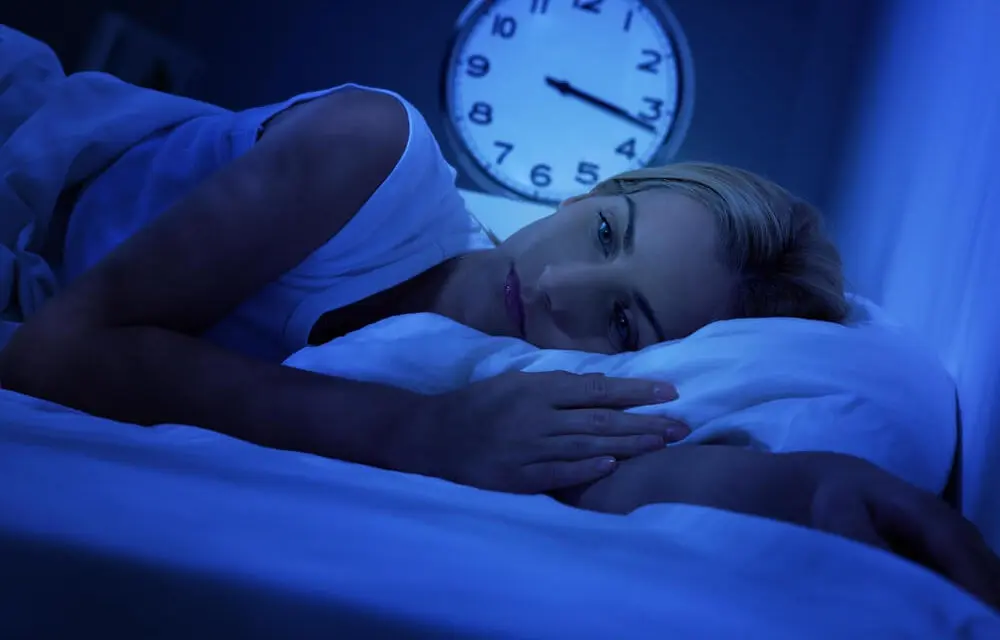 Woman lying in bed wide awake as the clock approaches 3:20 AM