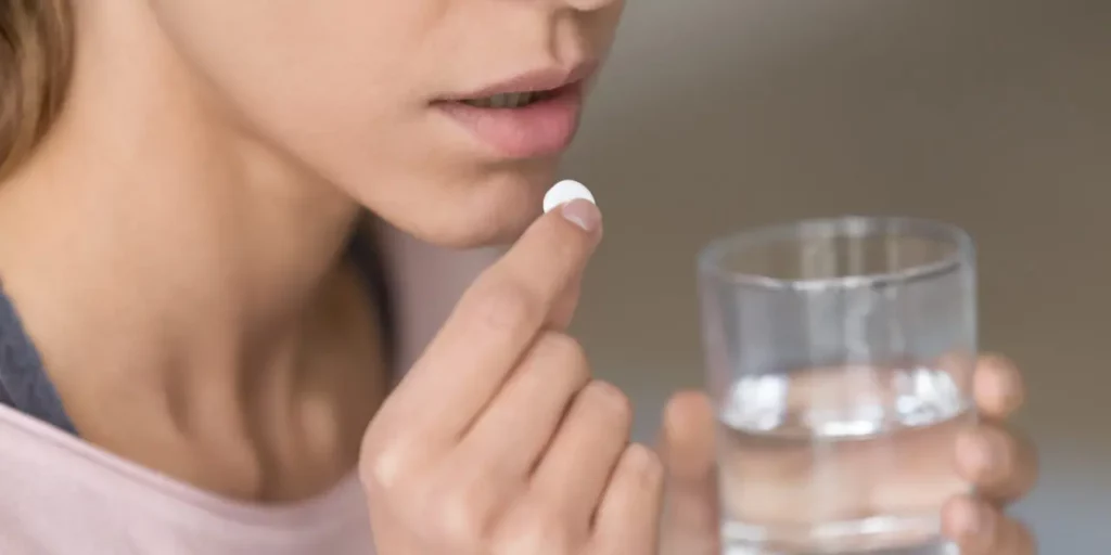 Women puts a pill in her mouth while holding a glass of water