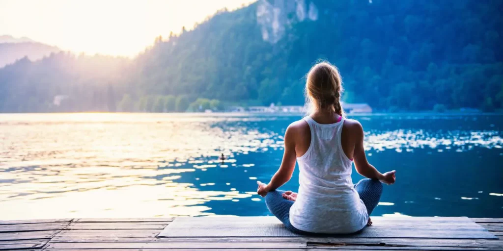 Women sits and meditates on a dock by a lake