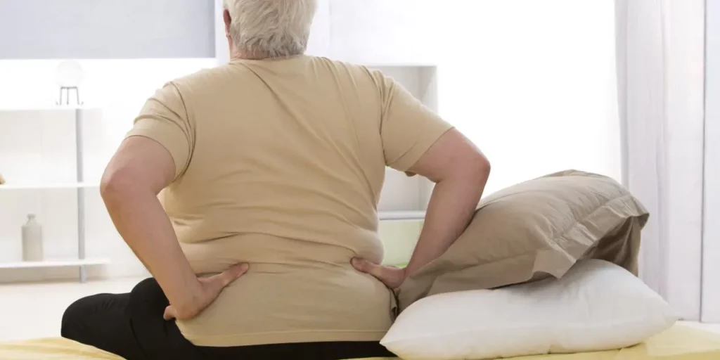 Overweight individual sits up from bed and puts hands on hips