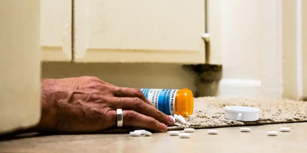 Pill bottle spilled as the hand of a man lies on the ground next to it, proving that painkillers can kill you