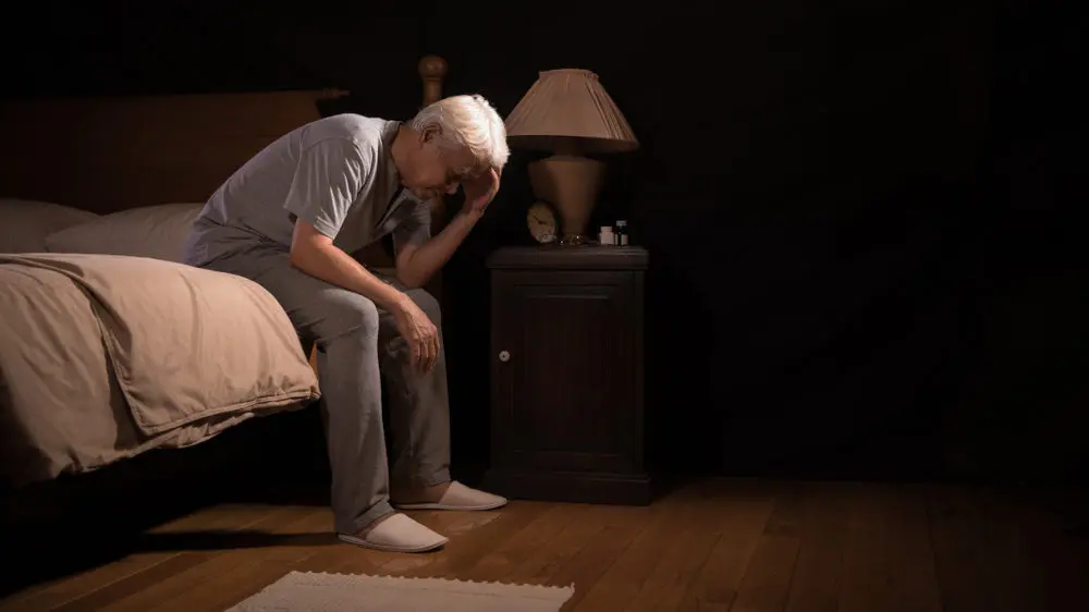 Man waking up in middle of the night and sitting up on the edge of bed exhausted